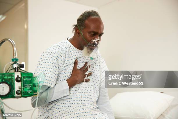patient touching chest wearing oxygen mask in medical room - nebulizador fotografías e imágenes de stock