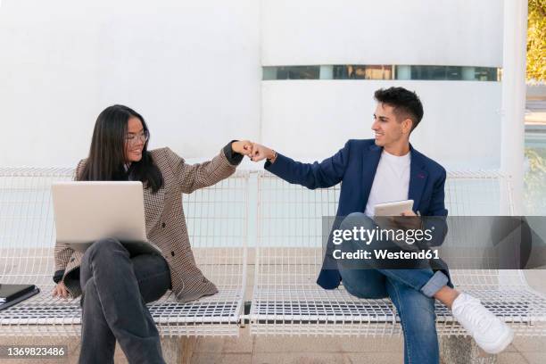 business colleagues giving fist bump sitting together on bench - fistbump stock-fotos und bilder