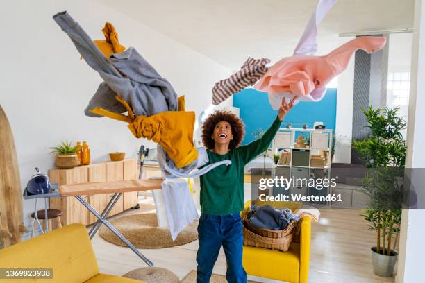 cheerful afro woman throwing clothes in living room at home - casalinga foto e immagini stock