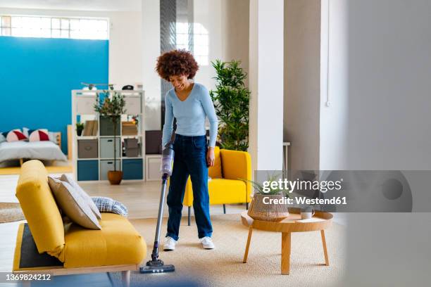 smiling young woman cleaning carpet in living room - vacuum cleaner stock pictures, royalty-free photos & images