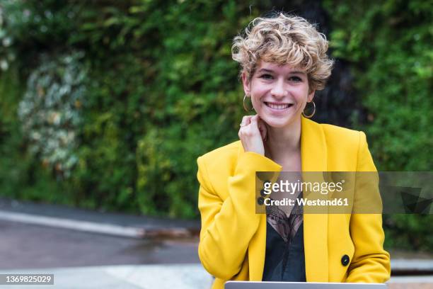 blond businesswoman sitting in park - veste jaune photos et images de collection