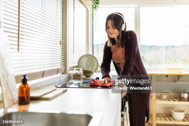 woman listening music cleaning induction stove in kitchen at home - burner stove top stockfoto's en -beelden