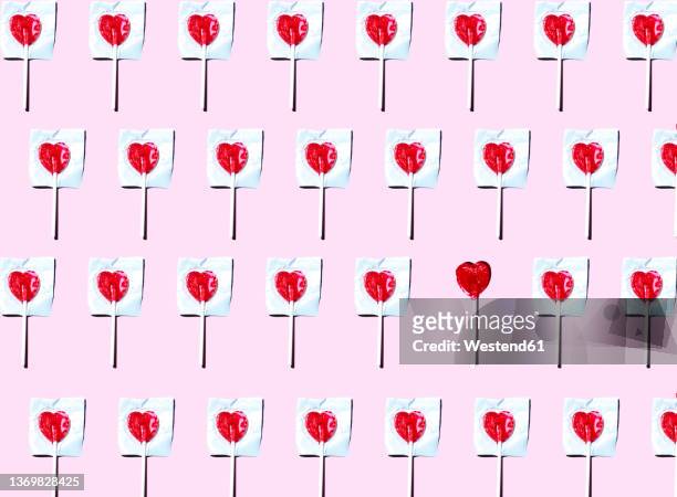 pattern of heart shaped lollipops flat laid against pink background with single one unwrapped - lollipop background stock pictures, royalty-free photos & images