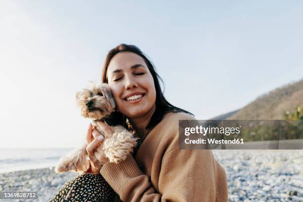 smiling young woman with eyes closed embracing yorkshire terrier at beach - dog eyes closed stock pictures, royalty-free photos & images