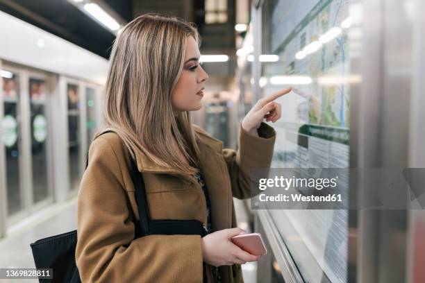 woman with smart phone pointing at map in underground station - femme metro photos et images de collection