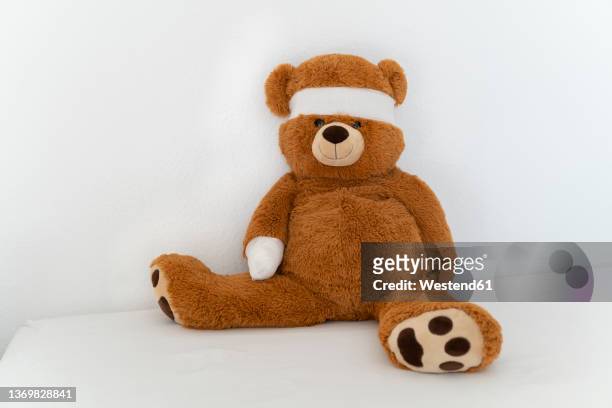 brown teddy bear with bandage on bed - teddybär stock-fotos und bilder