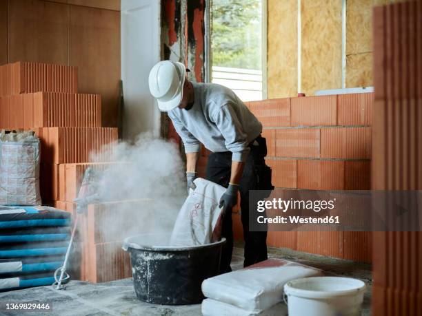 bricklayer putting cement in tub at construction site - zement stock-fotos und bilder