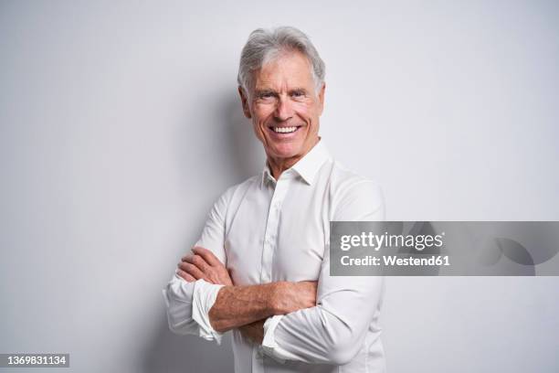 smiling senior businessman with arms crossed in front of white background - senior adult white background stock pictures, royalty-free photos & images