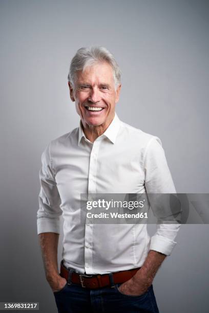 happy businessman with hands in pockets in front of gray background - weißes hemd freisteller stock-fotos und bilder