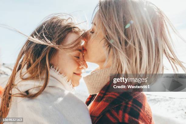 mother kissing daughter on forehead at beach - windswept stock pictures, royalty-free photos & images