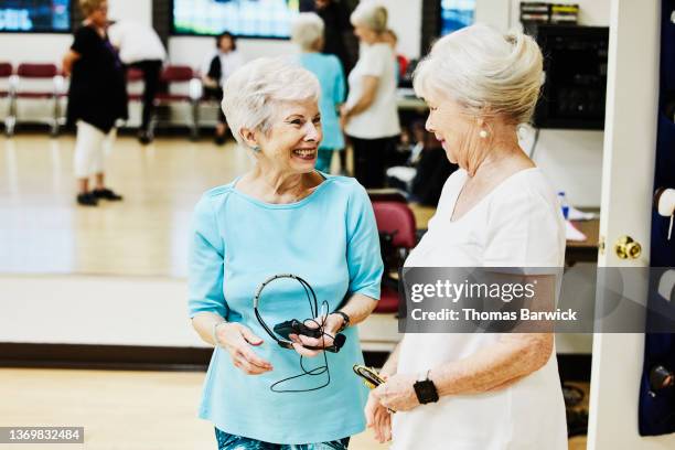 medium wide shot of smiling senior female friends in discussion before dance class in retirement community center - dancing studio shot stock pictures, royalty-free photos & images
