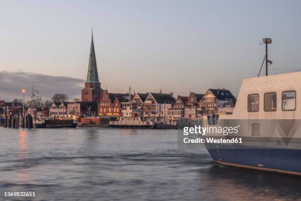 germany, schleswig-holstein, lubeck, skyline of travemunde at dusk with ferry in foreground - travemuende stock pictures, royalty-free photos & images