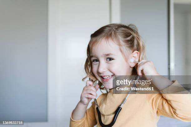 happy cute blond girl playing with stethoscope at home - auscultation child stock-fotos und bilder