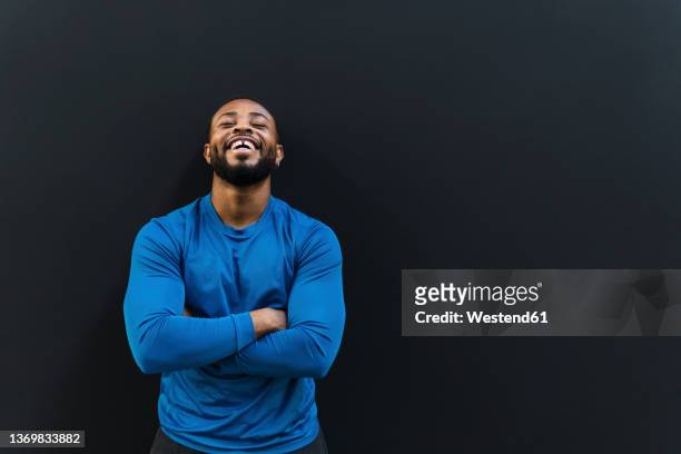 young athlete with arms crossed laughing against black background - three quarter length stock pictures, royalty-free photos & images