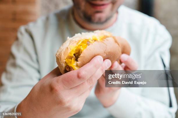 close up view of a man enjoying eating a delicious hot dog. - hot dog stock pictures, royalty-free photos & images