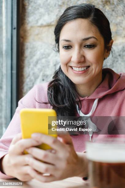 woman using a mobile phone while sitting in a brewery bar. - browsing the internet stock pictures, royalty-free photos & images