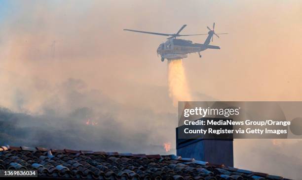 Laguna Beach, CA A helicopter makes a water drop on an early morning wind-driven fire burning near homes in the hills above Emerald Bay and Irvine...