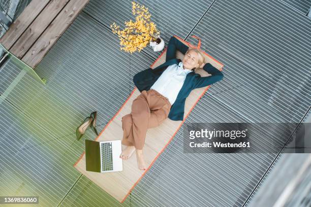 businesswoman lying on desk with laptop in office - hände hinter dem kopf stock-fotos und bilder
