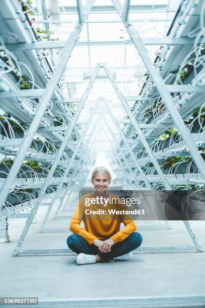 smiling agronomist sitting on ground at garden center - sitting on floor fotografías e imágenes de stock