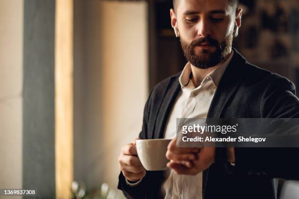 attractive adult bearded man indoors in cafe. lifestyle concept photo with copy space. picture of handsome guy with cup of beverage and smart watch - fancy coffee drink stock pictures, royalty-free photos & images