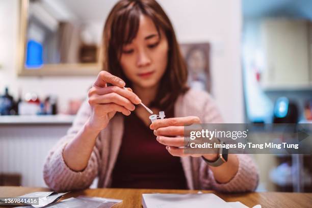 young pretty asian woman using covid-19 rapid self-test kit at home - coronavirus test stock pictures, royalty-free photos & images