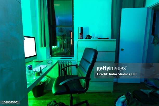 small apartment bedroom with desk and dresser is illuminated by green light. - small bedroom stock pictures, royalty-free photos & images