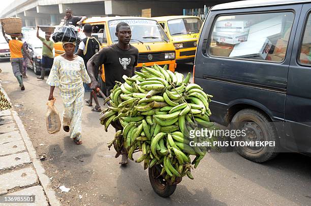 Woman accompanies a man carrying her plantain bananas to a car park at Mile 12 district in Lagos as labour suspend a five-day strike to dialogue with...