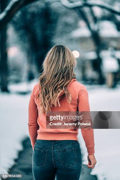 portrait from behind a casually dressed young caucasian woman wearing a hoodie standing on the sidewalk on a cold snowy day - back of womens heads stockfoto's en -beelden