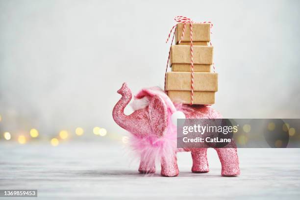 feiertagshintergrund mit rosa elefant, der eine weihnachtsmütze trägt und einen stapel geschenke zu weihnachten trägt - white elephant stock-fotos und bilder