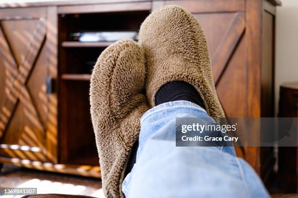 man's slippered feet on ottoman in front of out-of-frame tv - chinelo imagens e fotografias de stock