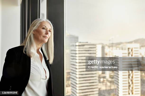 female ceo standing at office window and looking at city - three quarter front view 個照片及圖片檔