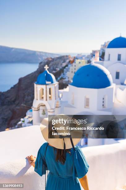 oia, santorini island, cyclades, greece. woman with hat watching cityscape, houses and churches - santorini - fotografias e filmes do acervo