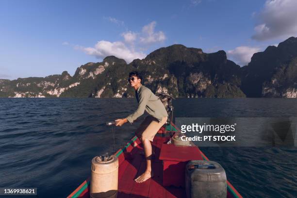 a man is sailing in a long-tail boat surrounded by mountains at cheow lan dam, khao sok, surat thani province. - nice weather stock pictures, royalty-free photos & images