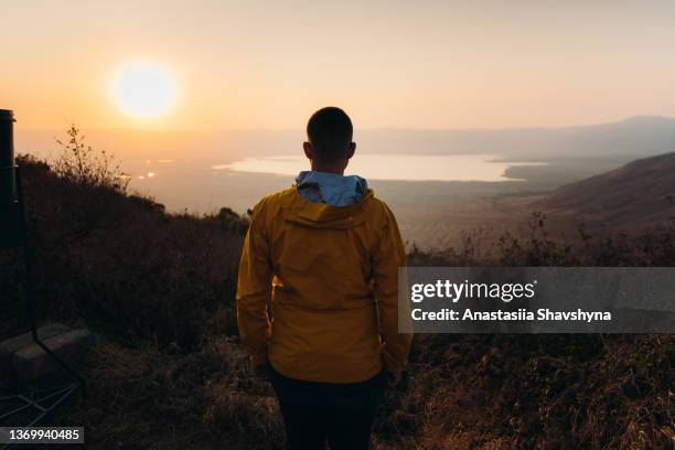 viaggiatore maschio che contempla l'alba panoramica sopra il cratere del vulcano ngorongoro in tanzania - ngorongoro foto e immagini stock