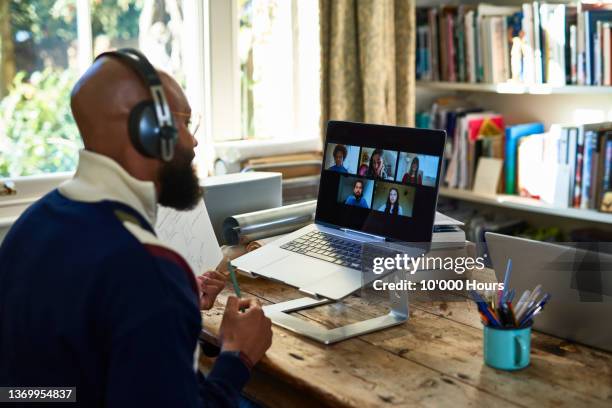 black entrepreneur wearing headphones on video conference call on laptop in home office - télétravail photos et images de collection