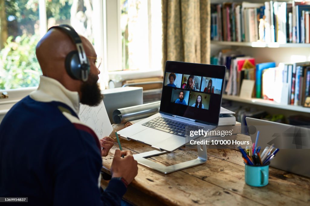 Black entrepreneur wearing headphones on video conference call on laptop in home office