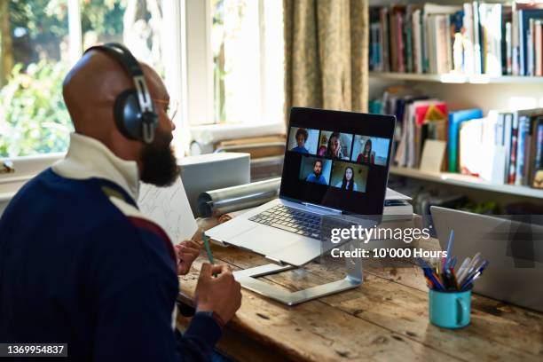 black entrepreneur wearing headphones on video conference call on laptop in home office - remote working stock pictures, royalty-free photos & images