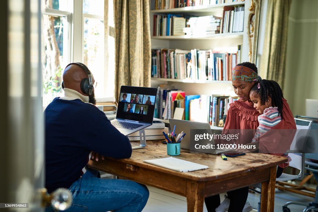 Two black parents with their young child working in home office