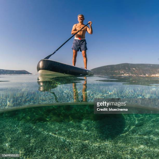 mature man on a paddleboard on the sea in summer - disruptagingcollection 個照片及圖片檔