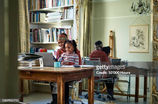 Black female entrepreneur sitting with child in front of laptop in home office
