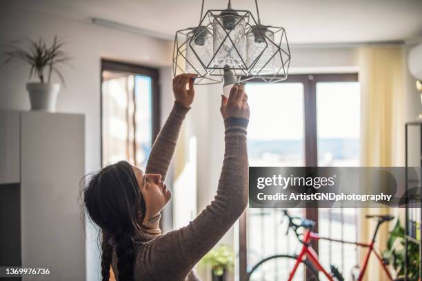woman changing energy efficient light bulb in living room. - installing ceiling light fixture stock pictures, royalty-free photos & images
