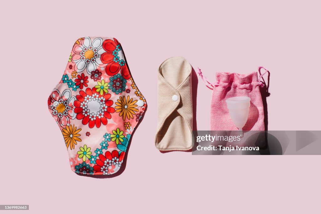 Reusable cloth menstrual pads and menstrual cup on pink background.
