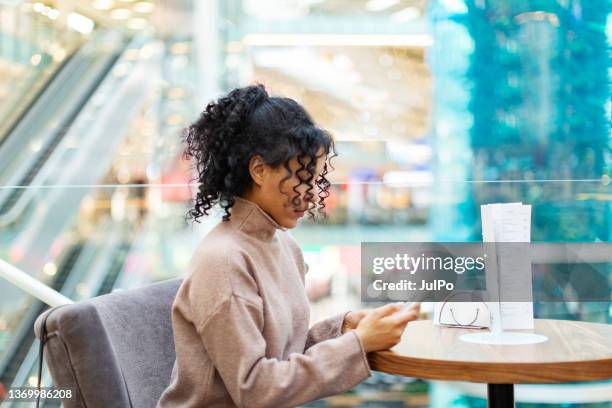 young african woman with mobile in cafe - african american restaurant texting stockfoto's en -beelden