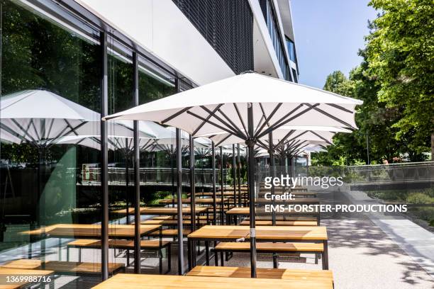 empty outdoor tables under white umbrella of a trendy restaurant - gartenschirm stock-fotos und bilder