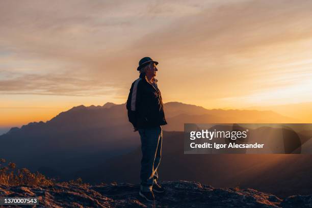 senior man enjoying sunset at the top of the mountain - old silhouette man stockfoto's en -beelden