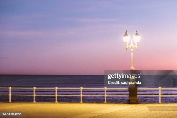 illuminated street lamp against the sea at dawn - gijon fotografías e imágenes de stock