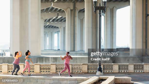 drei multirassische frauen laufen am wasser der stadt - heranlocken stock-fotos und bilder