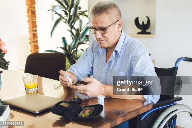 disabled senior man in a wheelchair uses a blood sugar test - medical test kit stock pictures, royalty-free photos & images