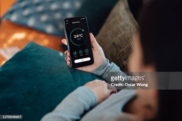 over the shoulder view of young woman using mobile app of smart home automation on smartphone. - temperature control stock pictures, royalty-free photos & images