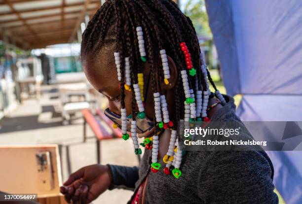 Young girl with braided hair and beads helps her mother February 5, 2022 at a fresh food stall on February 5, 2022 in Carriacou, Grenada. The island...